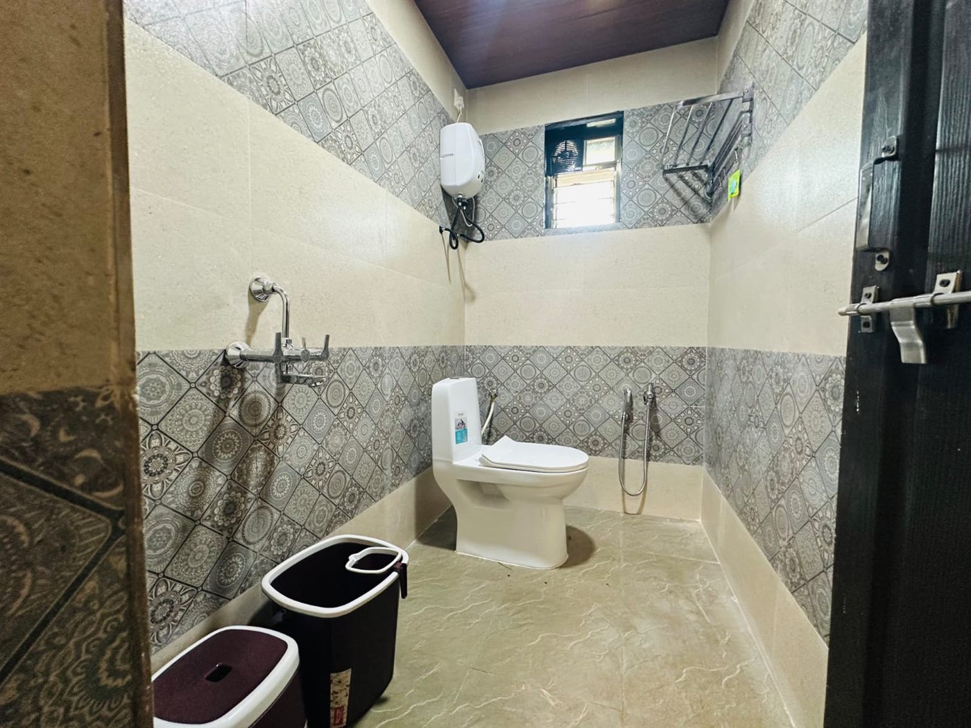 Supari bathroom with patterned grey tiles, western toilet, shower mixer and geyser