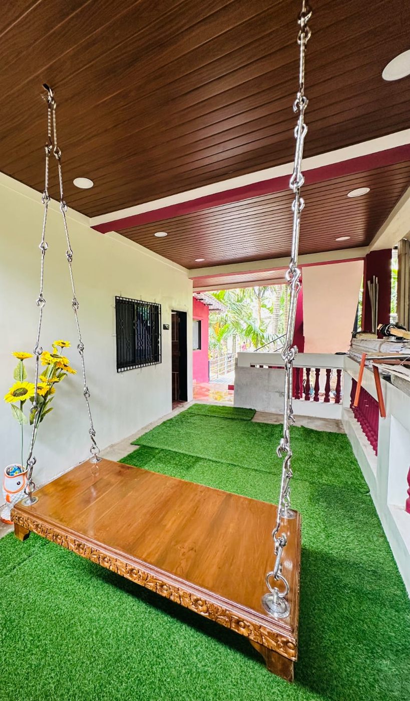 Carved wooden jhula swing on a green-carpeted verandah with a wood-panelled ceiling